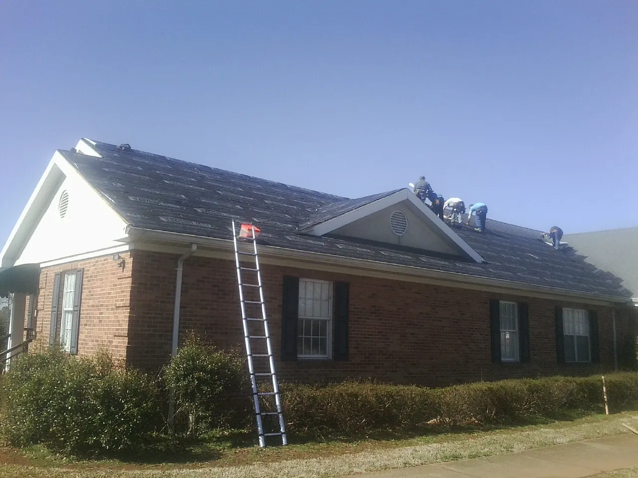 Crew tearing shingles off a brick ranch roof with a ladder set — Metal Roof Repair work by our crew in Westbrookville