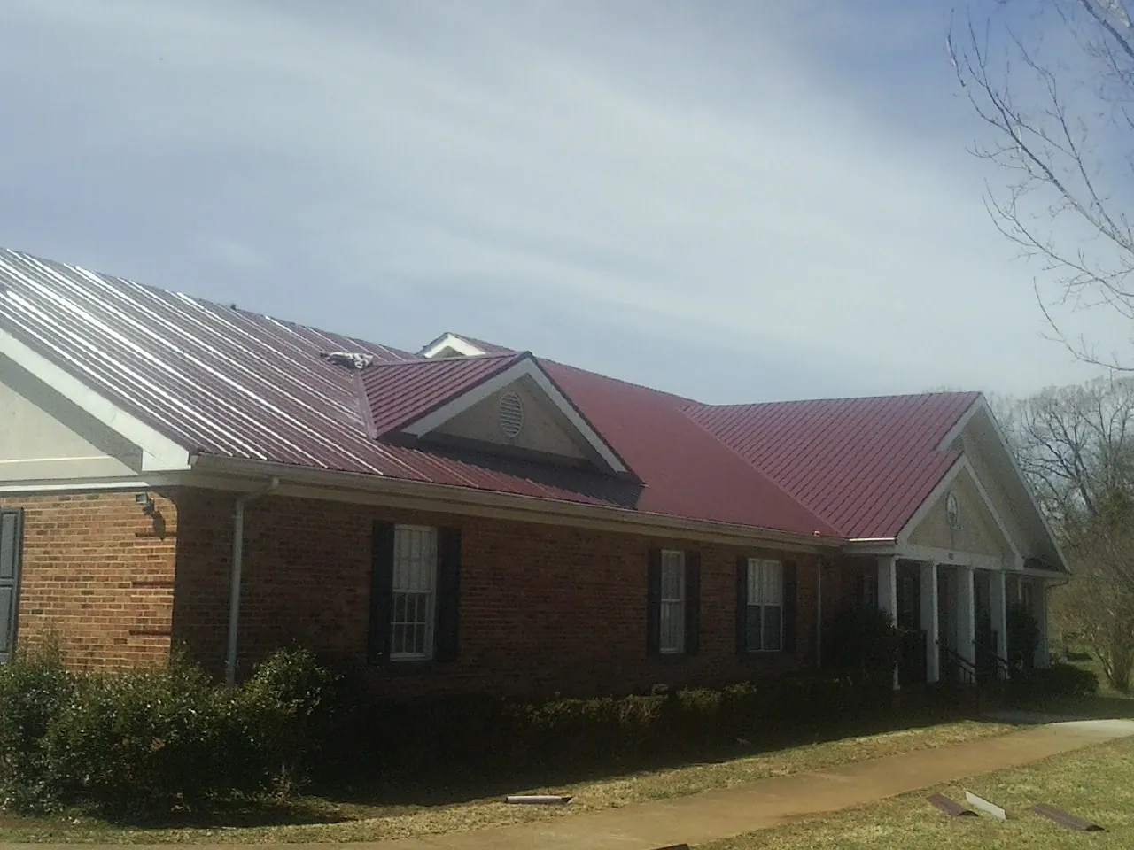 Red metal roof with gabled entries on a long brick building, from a Hail Damage Roof Repair job in Westbrookville