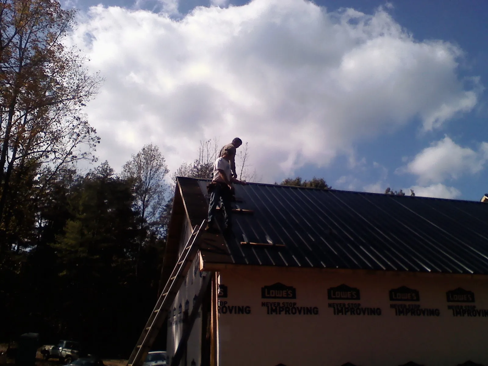 Roofer fastening dark metal panels high against a cloudy sky, from a Roof Inspection job in Westbrookville