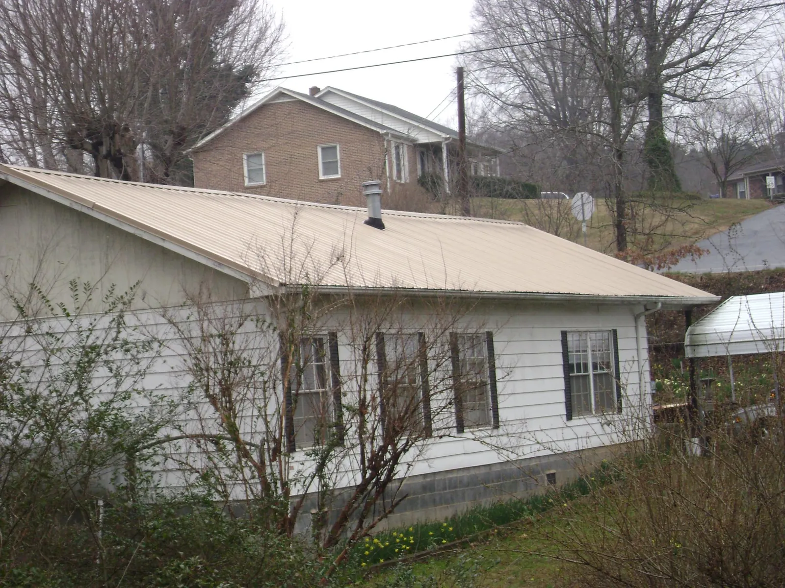 Tan metal roof on a white sided house set into a hillside — Commercial Roofing by Roofing Brothers in Westbrookville